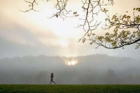 A person runs on the 雅典 bike path with a sunset peeking through the clouds in the background